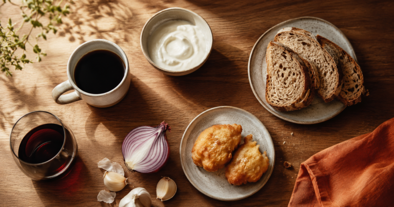 Flat lay of common IBS trigger foods on a wooden table: coffee, red wine, onion, garlic, fried food, bread and dairy